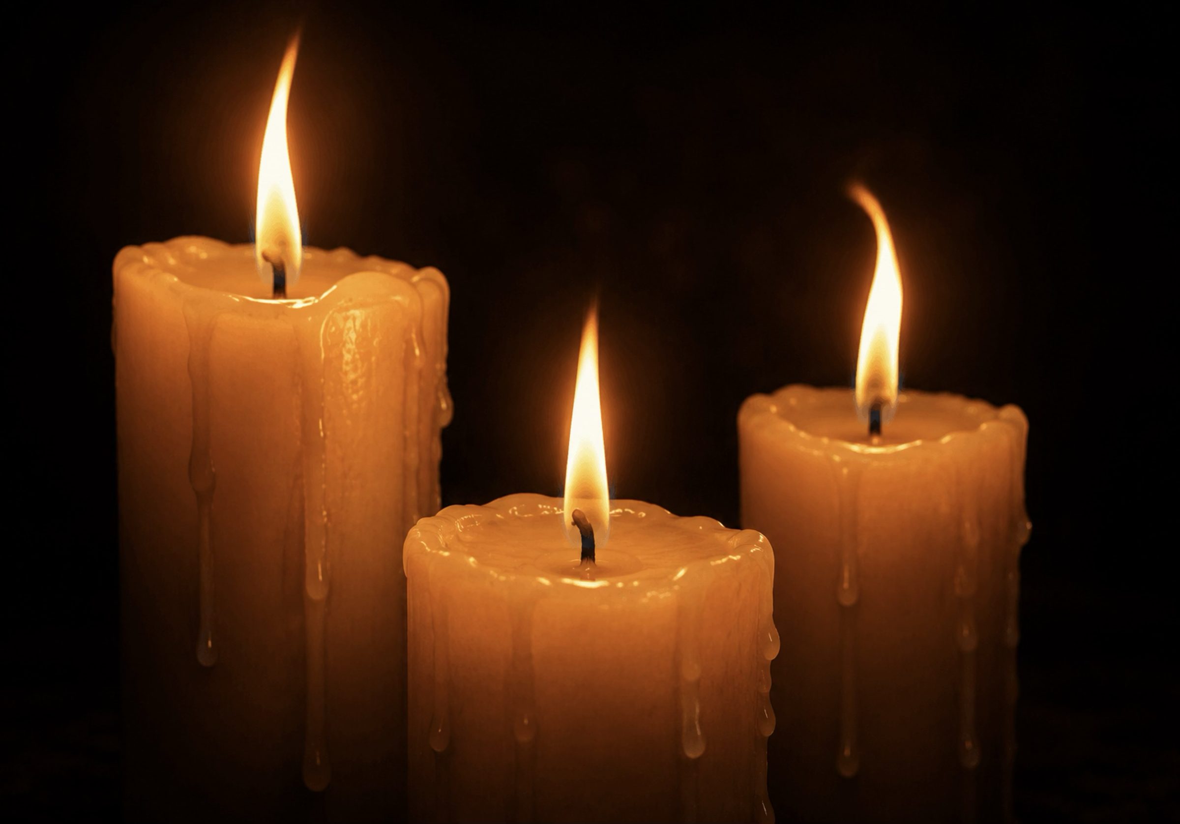 Three lit candles burning in darkness, representing remembrance of the victims of violence in the Democratic Republic of Congo
